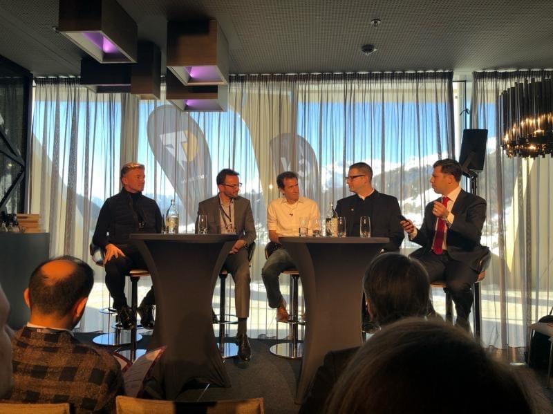 Eric Kryski speaking on a panel at Davos with the Alps behind the windows.