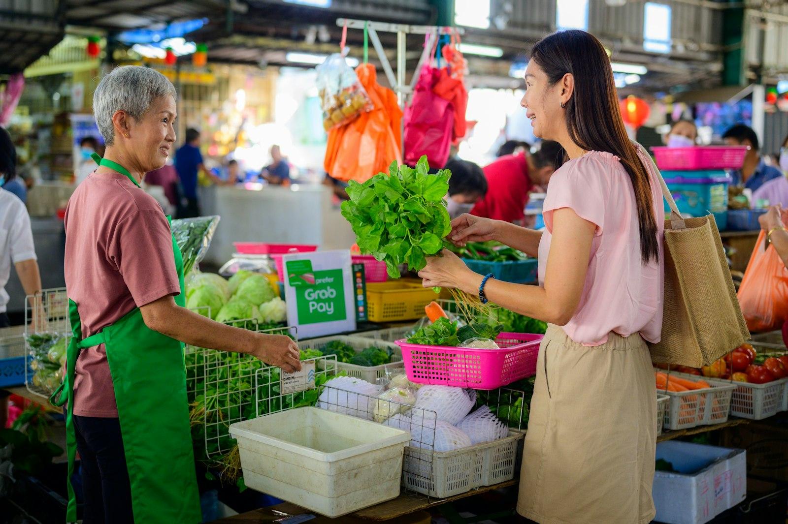 A woman buying fresh greens from a vendor at a Southeast Asian market